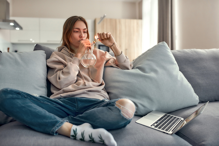 Woman lighting a bong while sitting in the couch