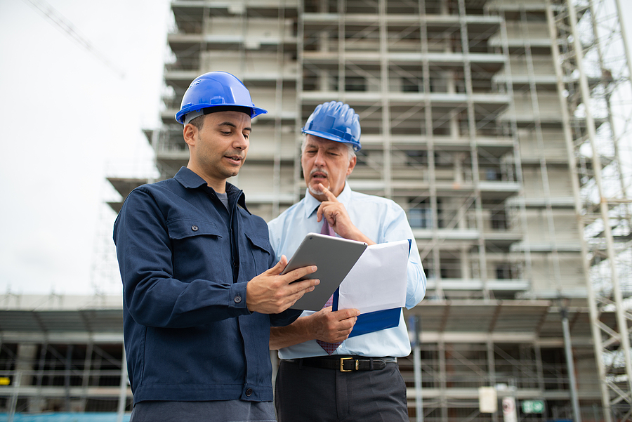 Architect and site manager using construction project management software in a tablet